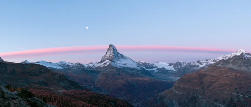 Matterhorn mountain peak at twilight with snow and autumn forest in alpine valley