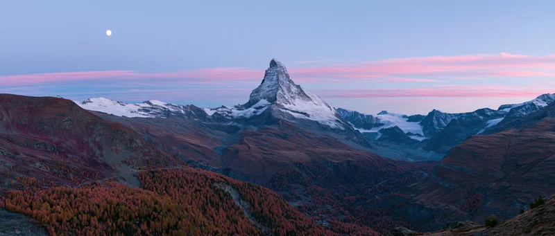 Matterhorn peak rising above autumn-colored larch forest in alpine valley at twilight