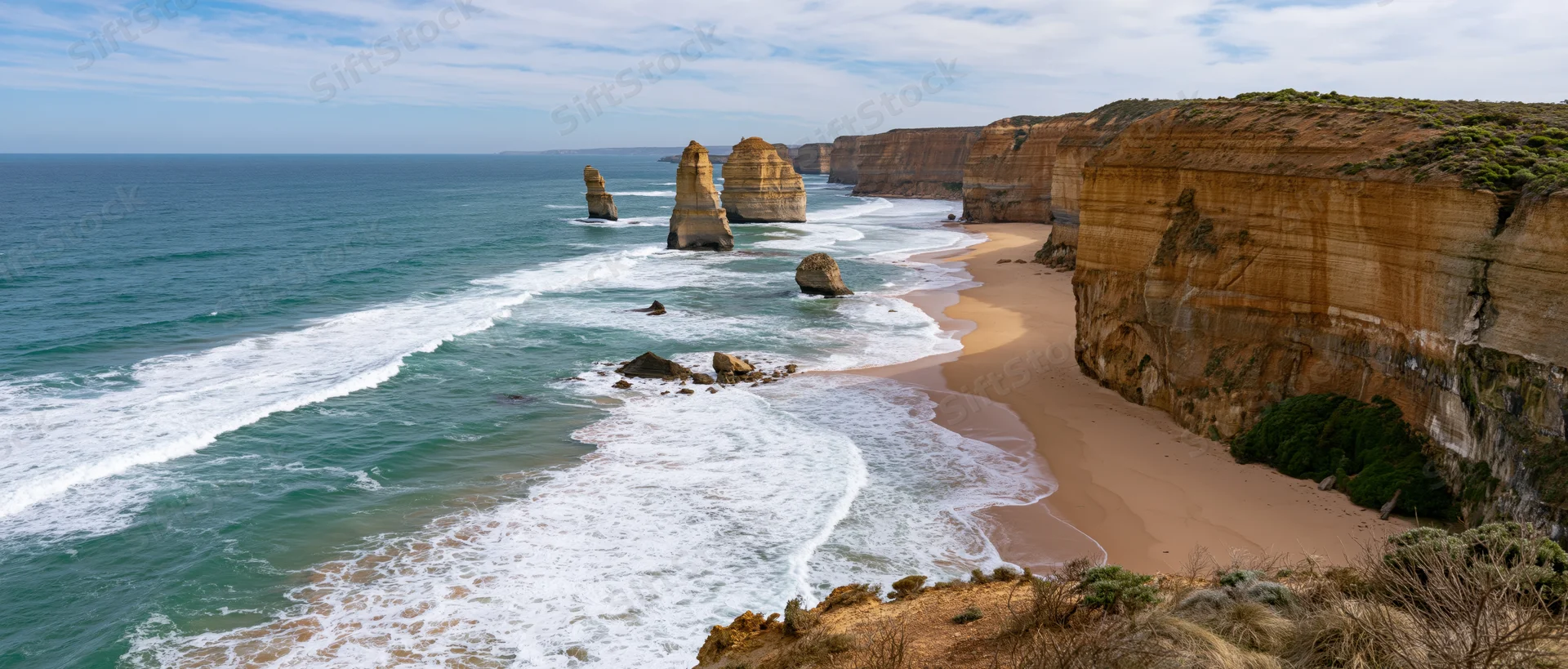 Sea stacks and cliffs along a sandy beach with waves crashing under a blue sky