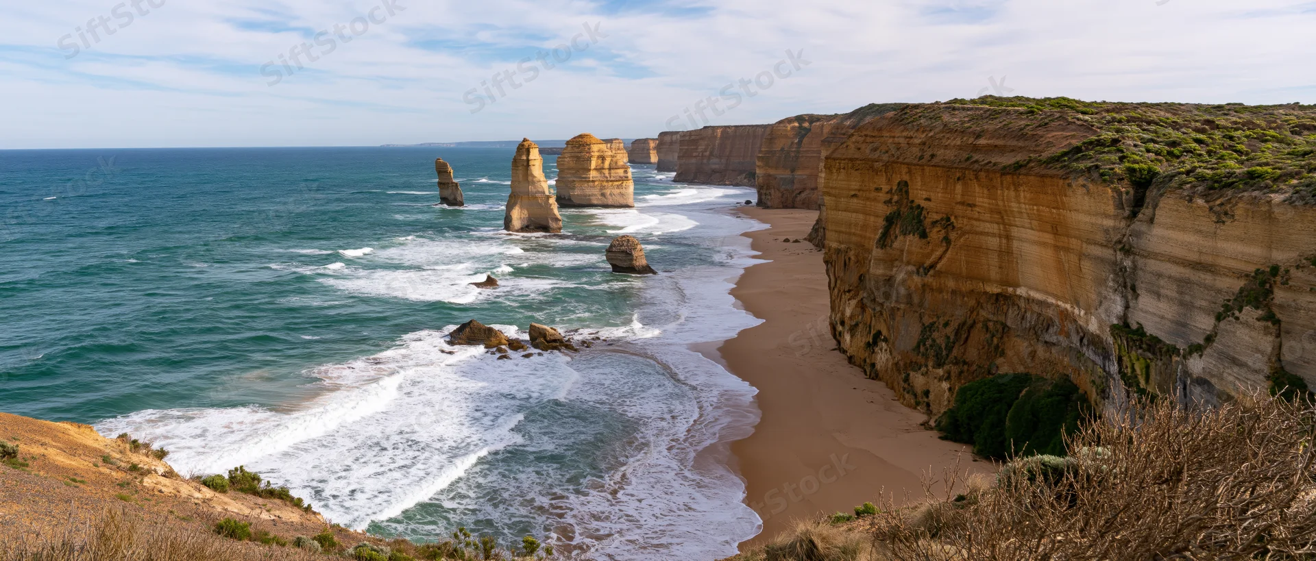 Sea stacks and cliffs along a sandy beach with waves crashing at the shore