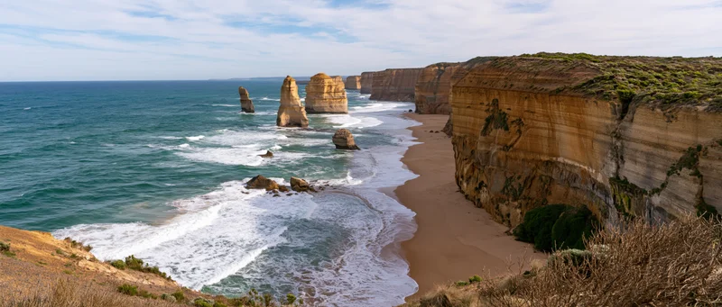 Sea stacks and cliffs along a sandy beach with waves crashing at the shore