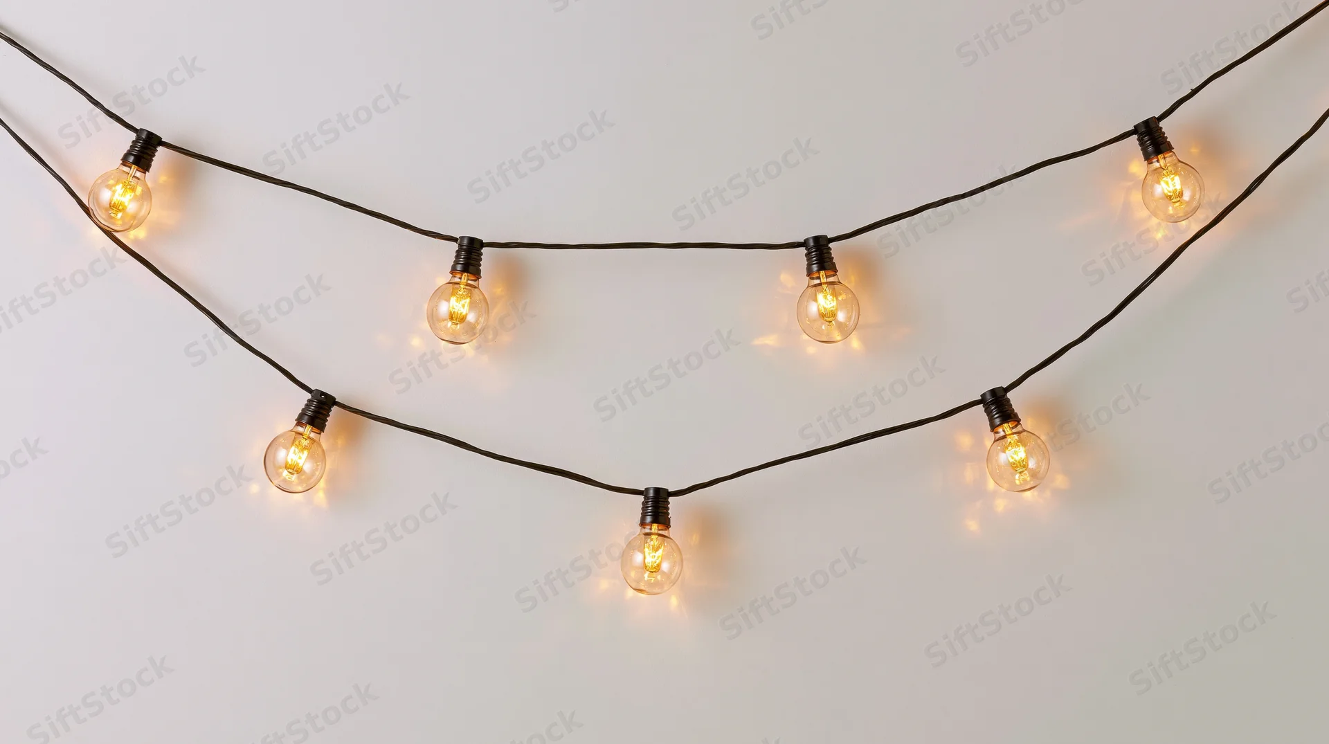 String of warm glowing bulbs hanging in a curved arrangement against a plain wall