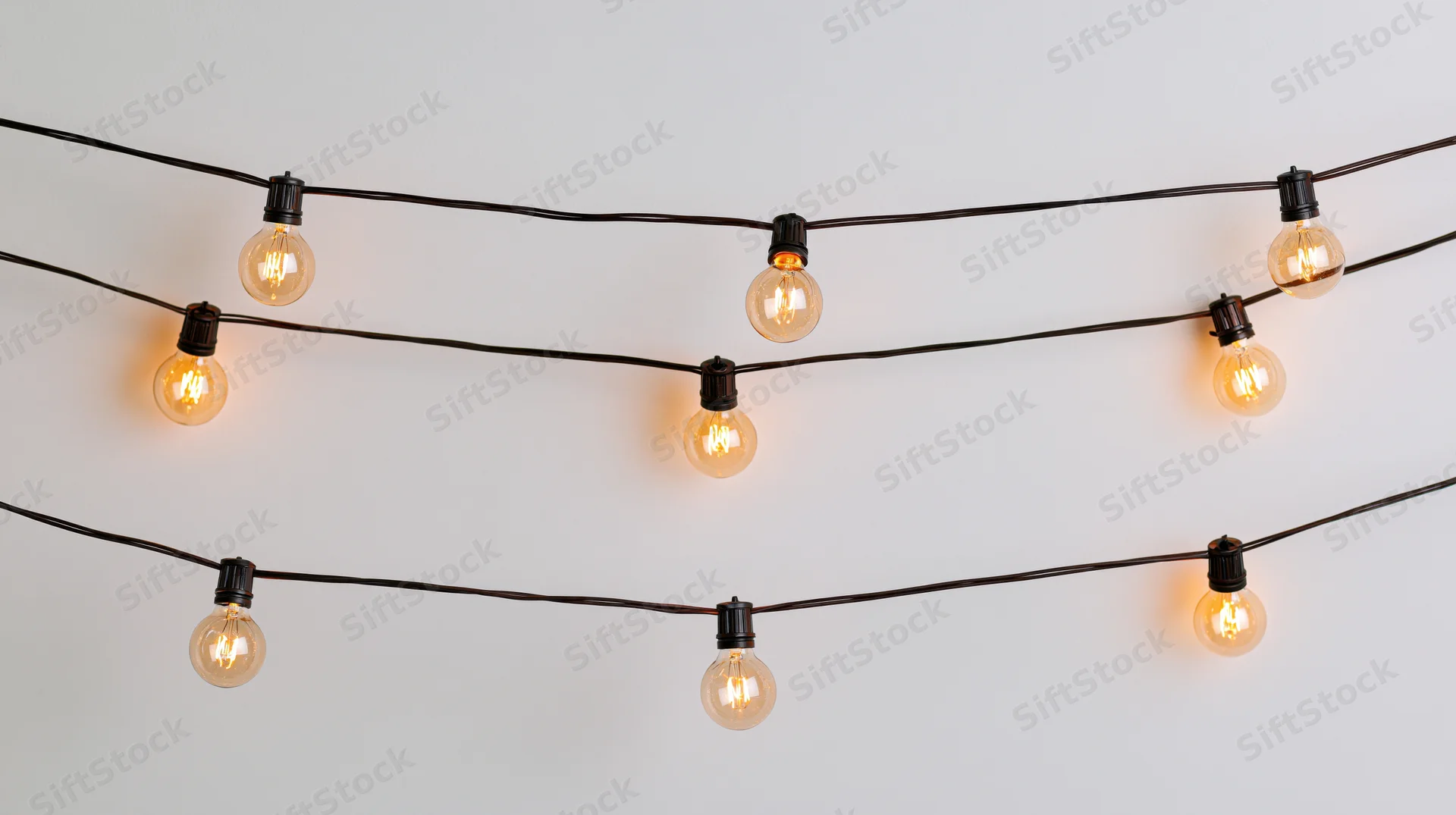 String lights with warm glowing bulbs arranged in parallel rows against a plain white wall