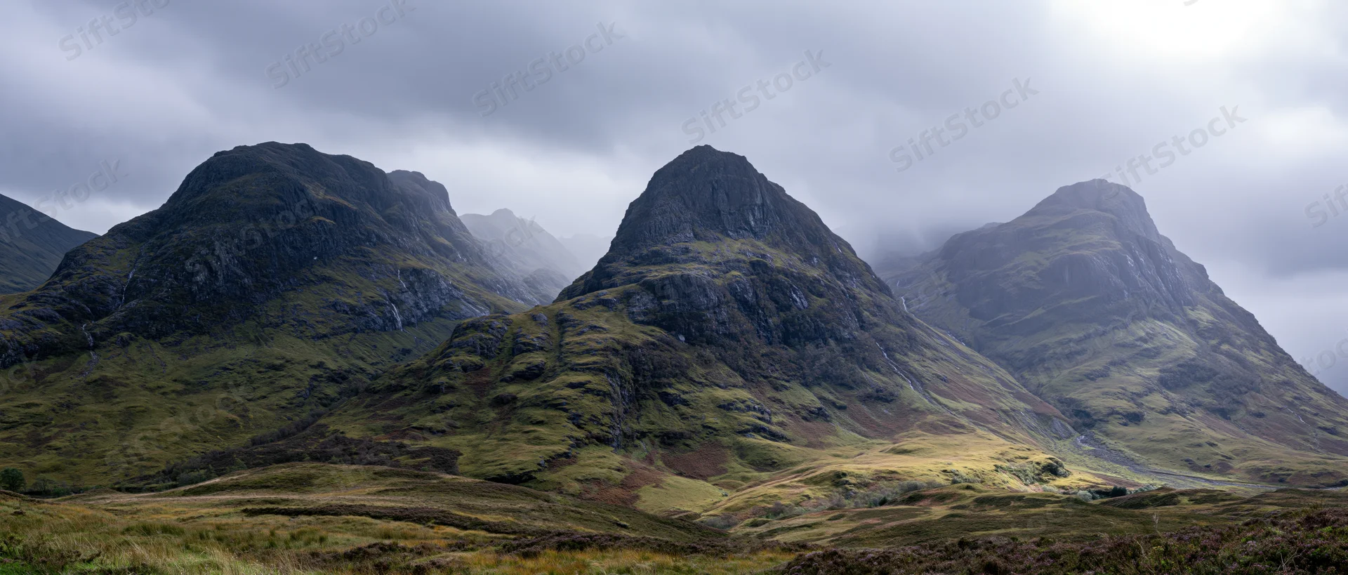 Rugged mountain peaks rising from a grassy moor under cloudy skies in the Scottish Highlands