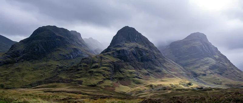 Rugged mountain peaks rising from a grassy moor under cloudy skies in the Scottish Highlands