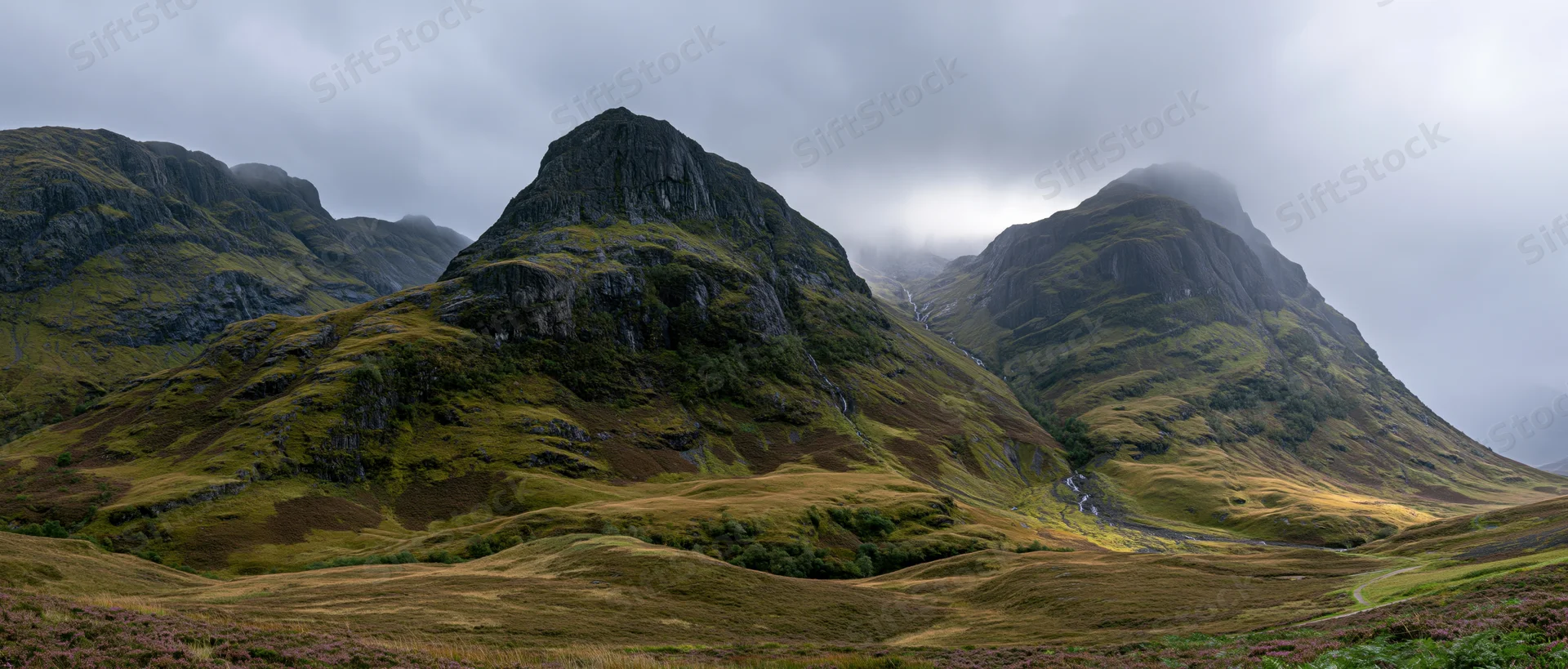 Rugged mountain peaks rising over a grassy valley under cloudy skies in the scottish highlands
