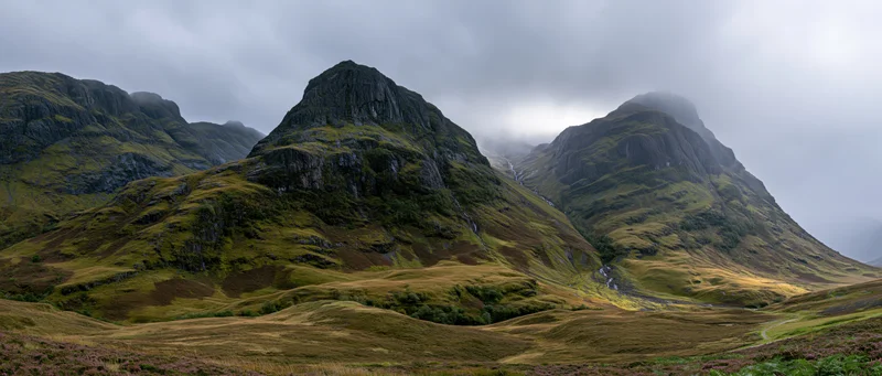 Rugged mountain peaks rising over a grassy valley under cloudy skies in the scottish highlands