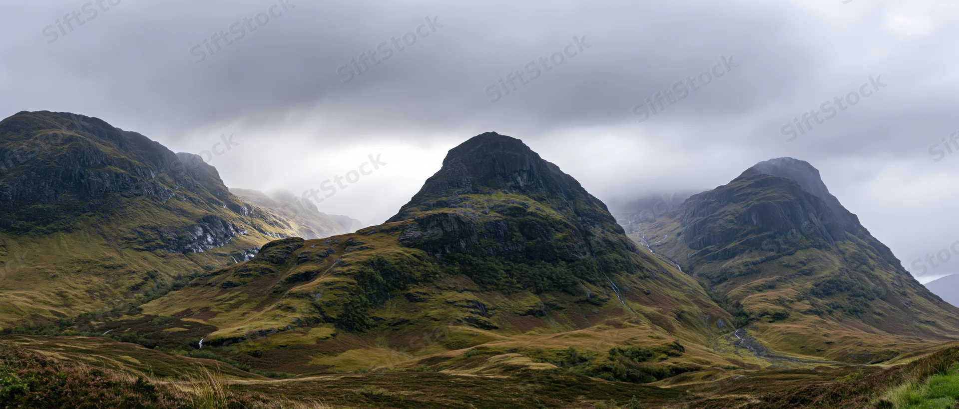 Rugged mountain peaks rising from a grassy valley under an overcast sky in the Scottish Highlands