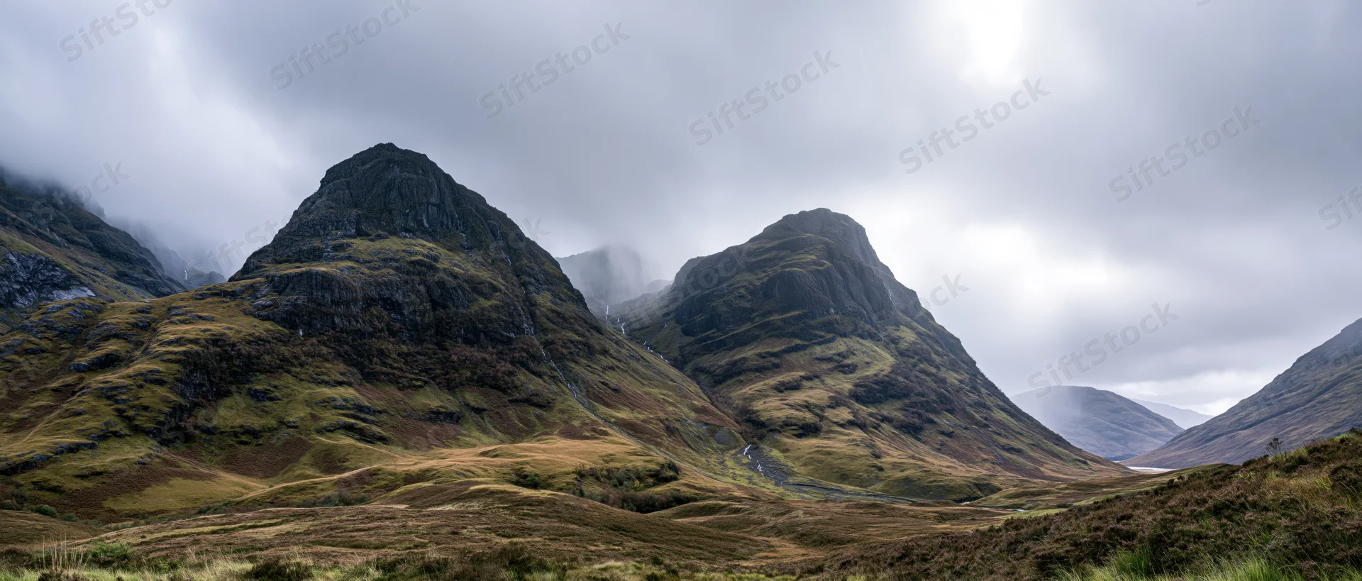 Rugged mountain peaks rising from a grassy valley under an overcast sky in the Scottish Highlands