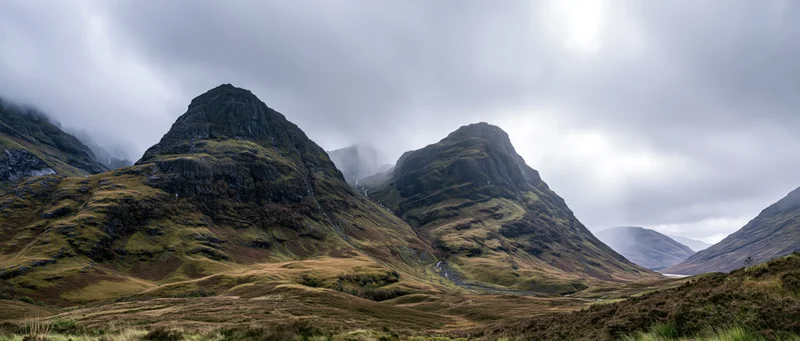 Rugged mountain peaks rising from a grassy valley under an overcast sky in the Scottish Highlands