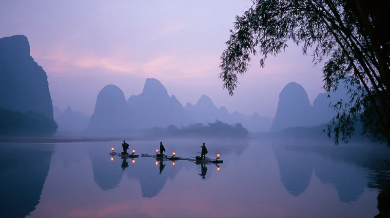 Fishermen on bamboo rafts fishing at twilight on a misty river with karst mountains reflected in the water