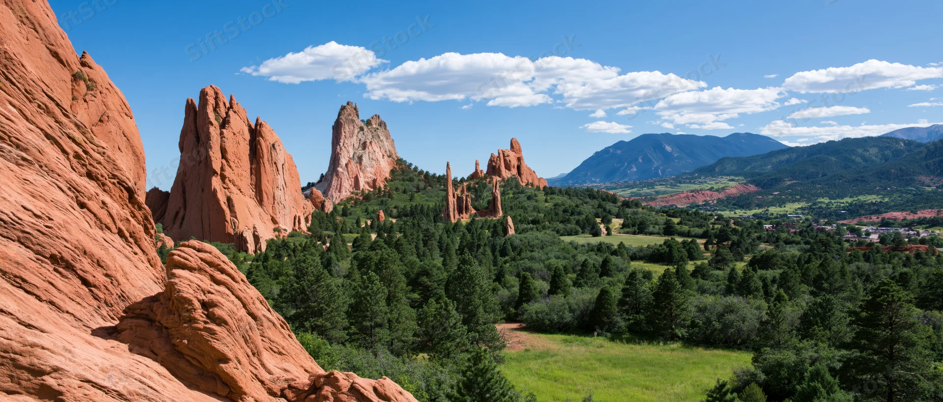 Red rock formations rising from a forested valley under a blue sky with scattered clouds