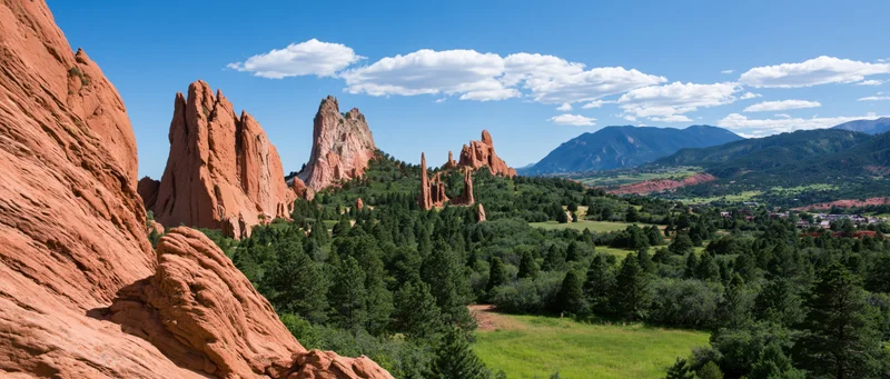 Red rock formations rising from a forested valley under a blue sky with scattered clouds