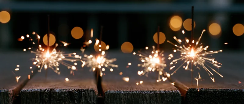 Sparklers burning on a wooden surface at night with bokeh lights in the background