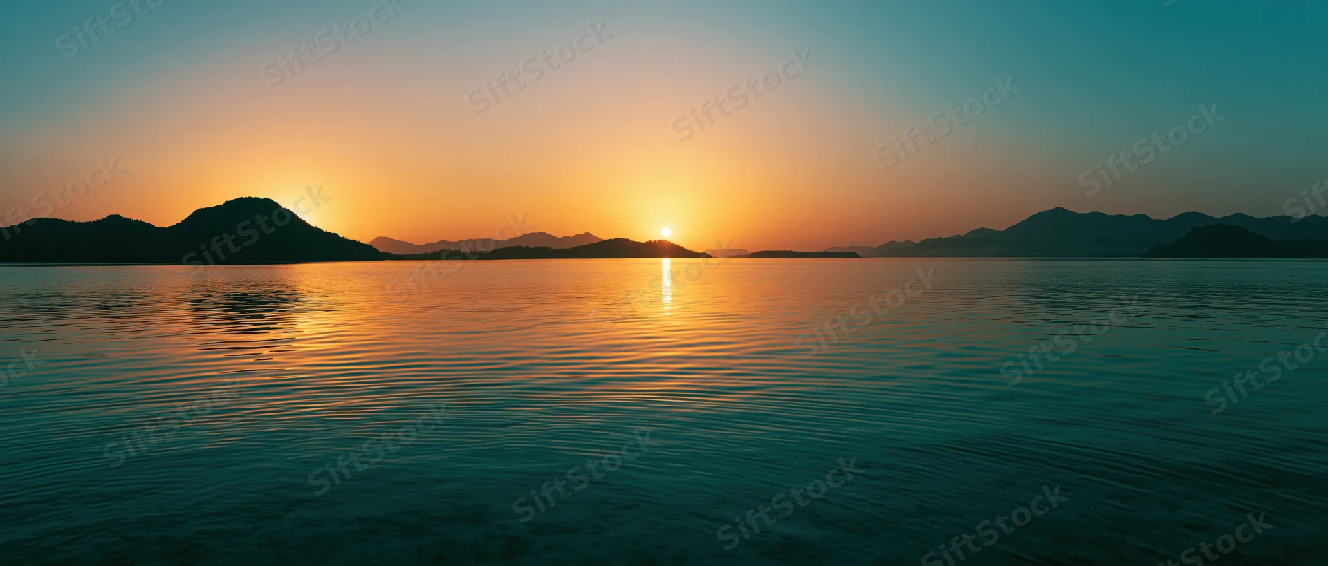 Sunset over calm lake reflecting golden light with mountain silhouettes on horizon