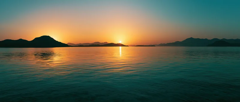 Sunset over calm lake reflecting golden light with mountain silhouettes on horizon
