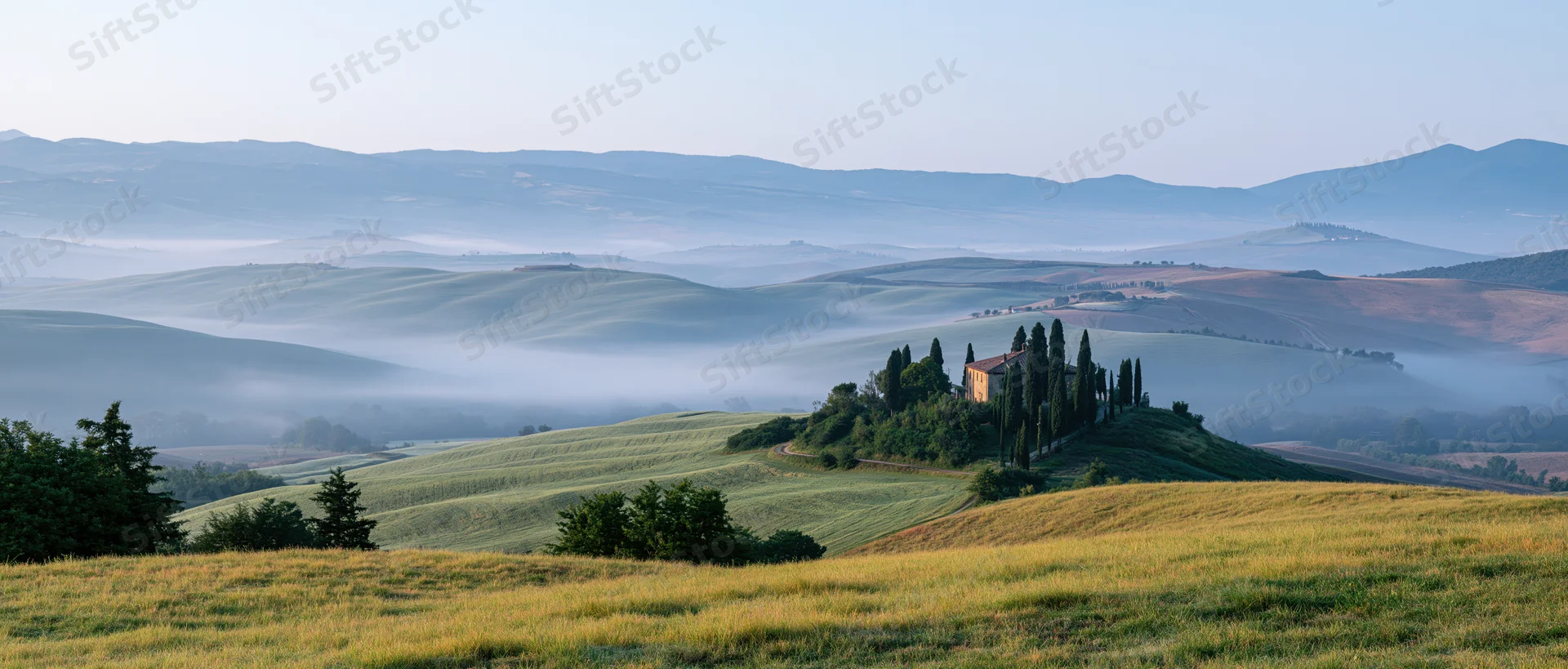 Villa on a hill surrounded by rolling green fields and misty valleys in tuscany at sunrise