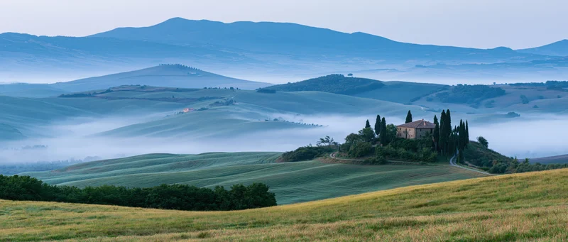 Villa on a hill surrounded by foggy rolling fields in tuscany at dawn