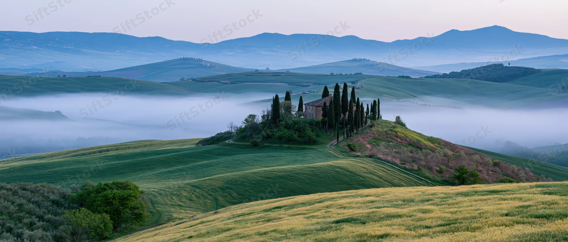 A villa surrounded by cypress trees on a hilltop in the misty tuscany countryside at sunrise