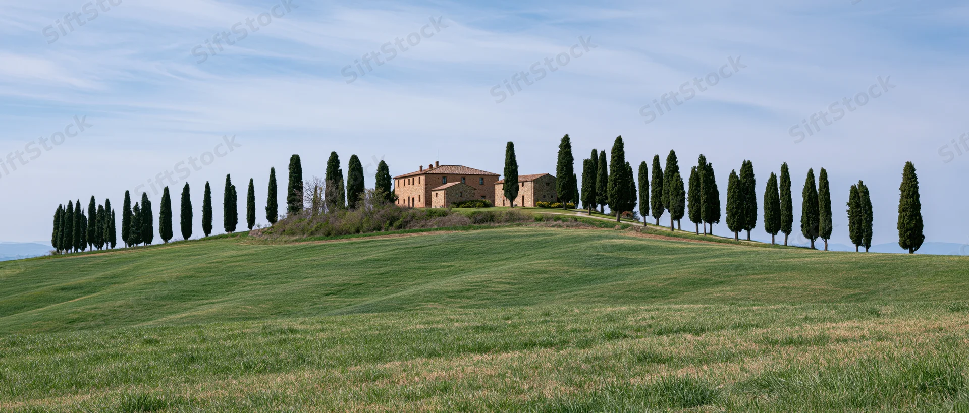 Tuscan villa on a grassy hill surrounded by cypress trees under a blue sky