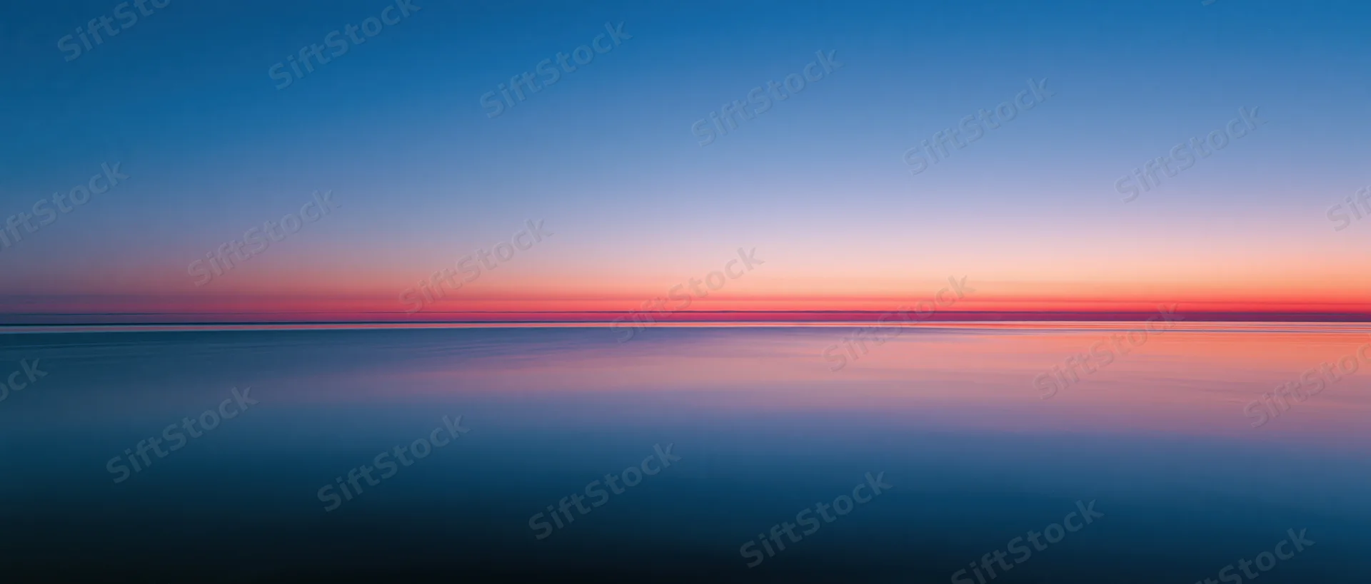 Calm ocean surface reflecting sunset sky at twilight