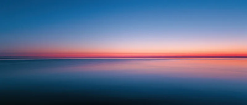 Calm ocean surface reflecting sunset sky at twilight