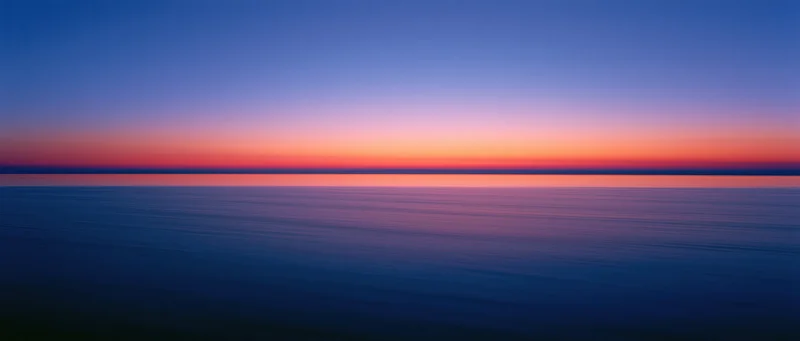 Calm ocean surface reflecting sunset sky at twilight horizon