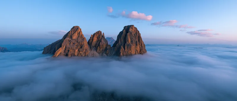 Jagged mountain peaks rising above a sea of clouds at dawn