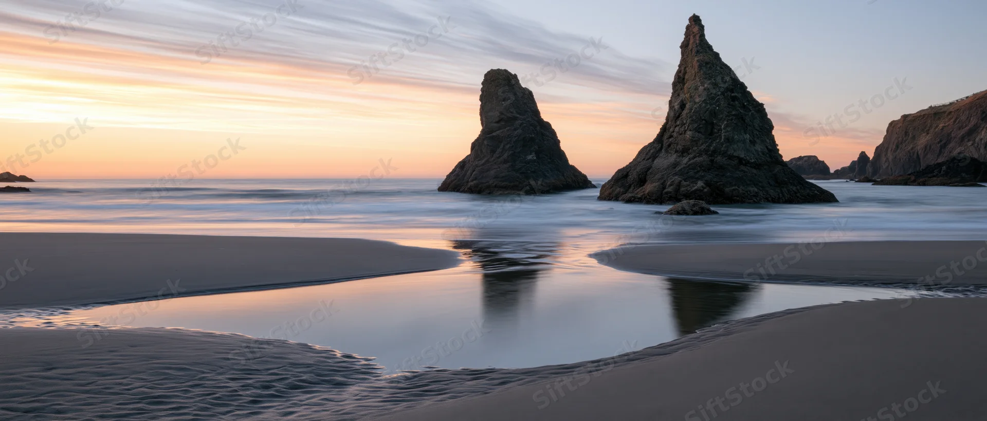 Sea stacks rising from calm ocean at sunset on sandy beach