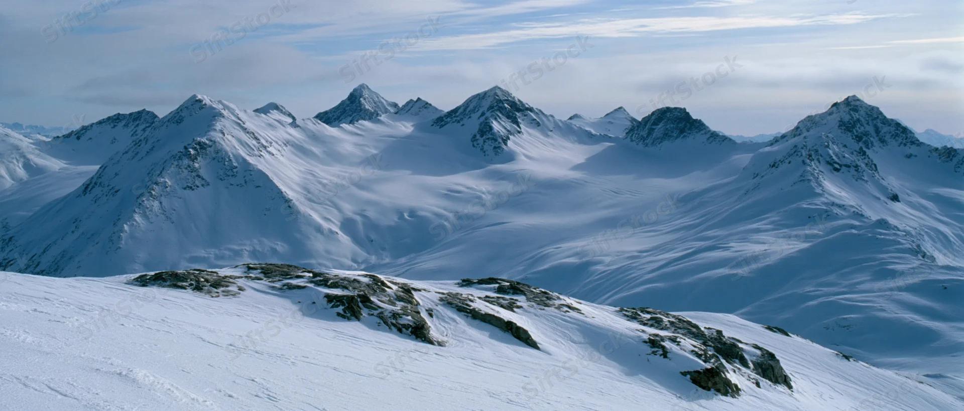 Snow-covered mountain peaks and glaciers in alpine terrain under a partly cloudy sky