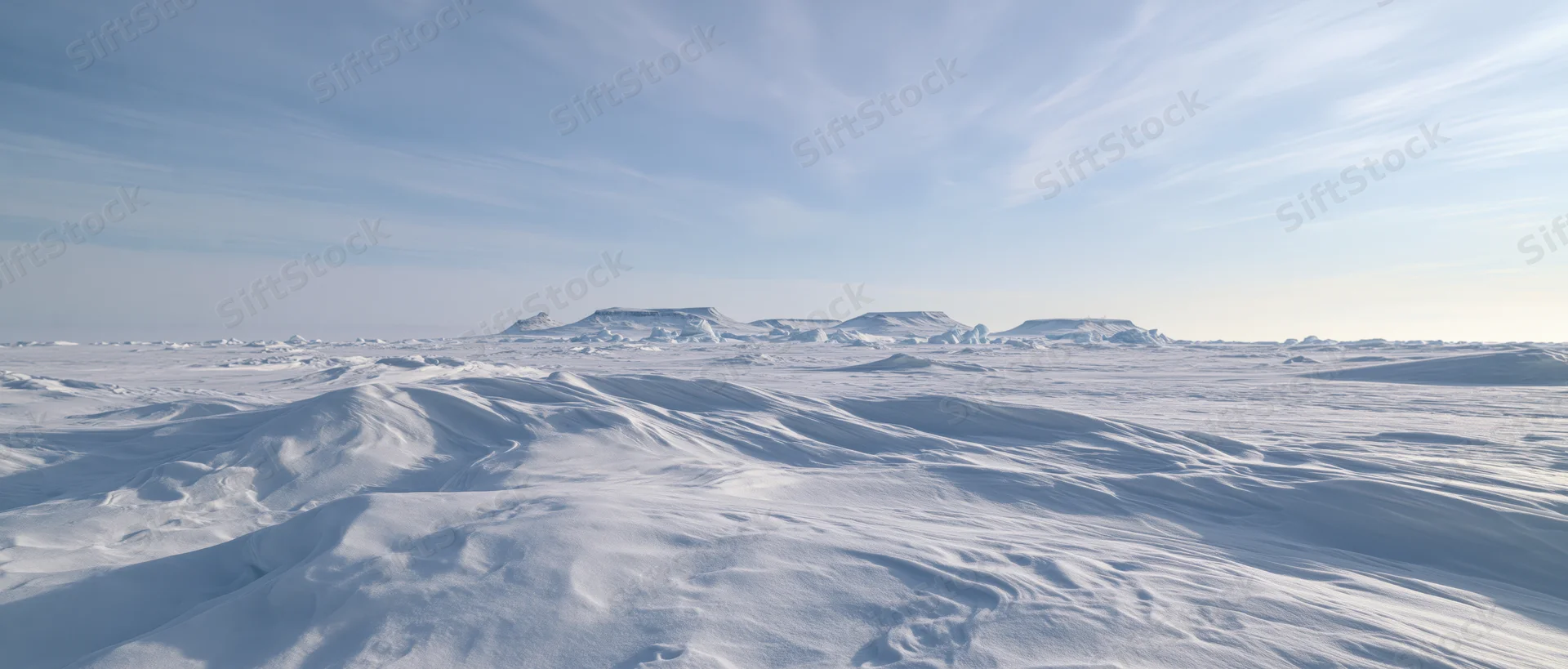 Snow-covered arctic tundra with distant ice plateaus under a pale blue sky