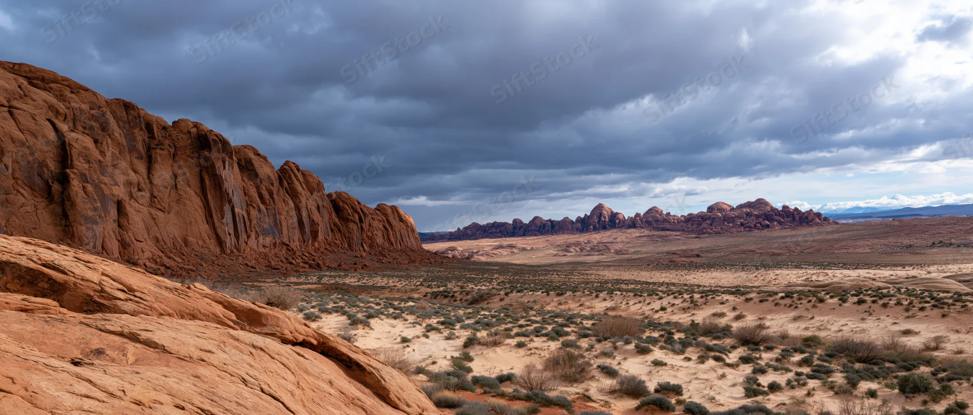 Red rock formations and desert valley under stormy sky in arid landscape