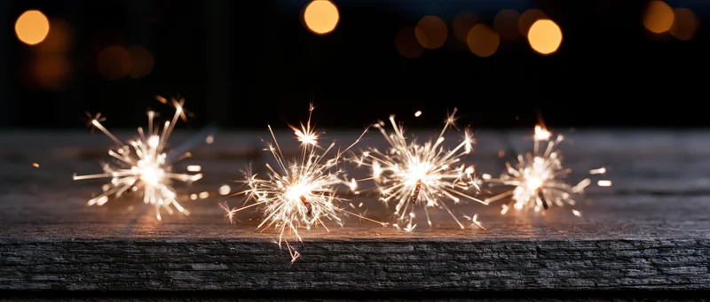 Sparklers burning on a wooden surface at night with bokeh lights in the background