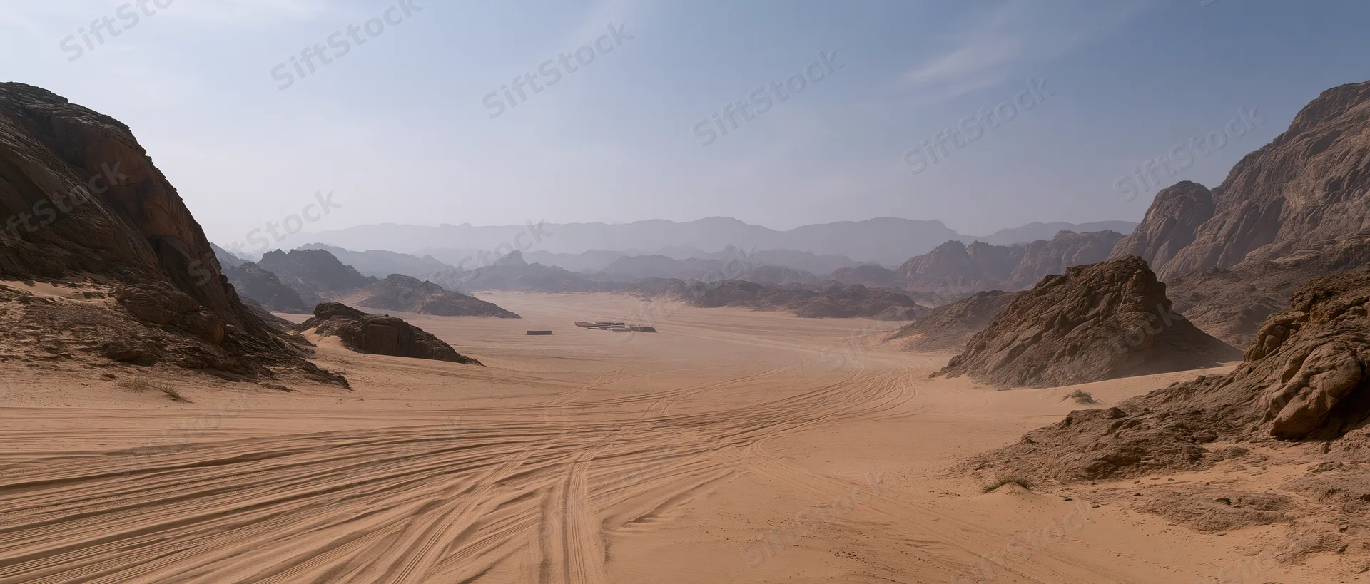 Desert valley with sand dunes and rocky mountains under clear sky, tire tracks leading into distance