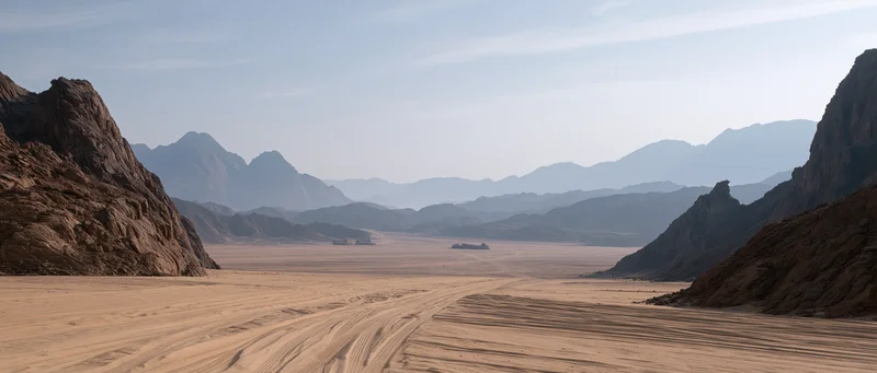 Desert valley with rocky mountains and sand dunes under a hazy blue sky