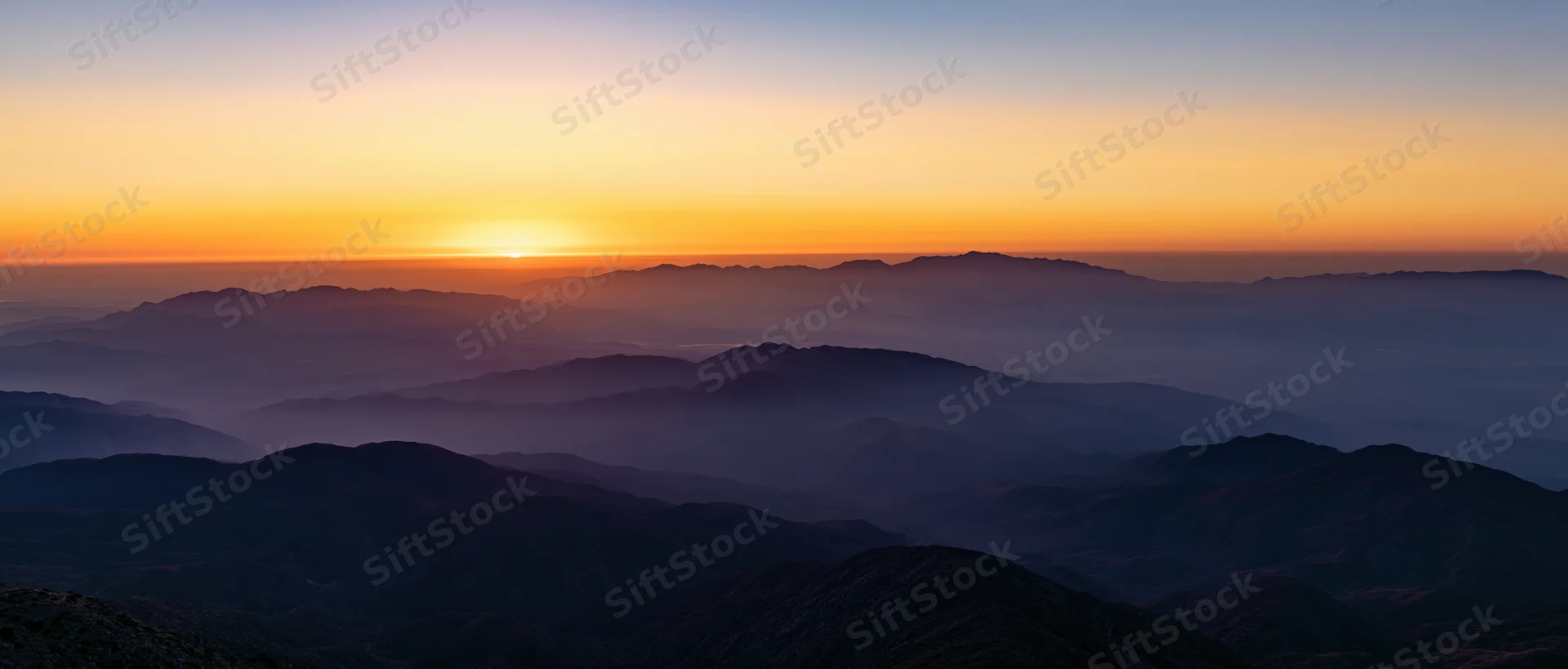 Layered mountain ridges silhouetted against a sunrise sky with mist filling the valleys