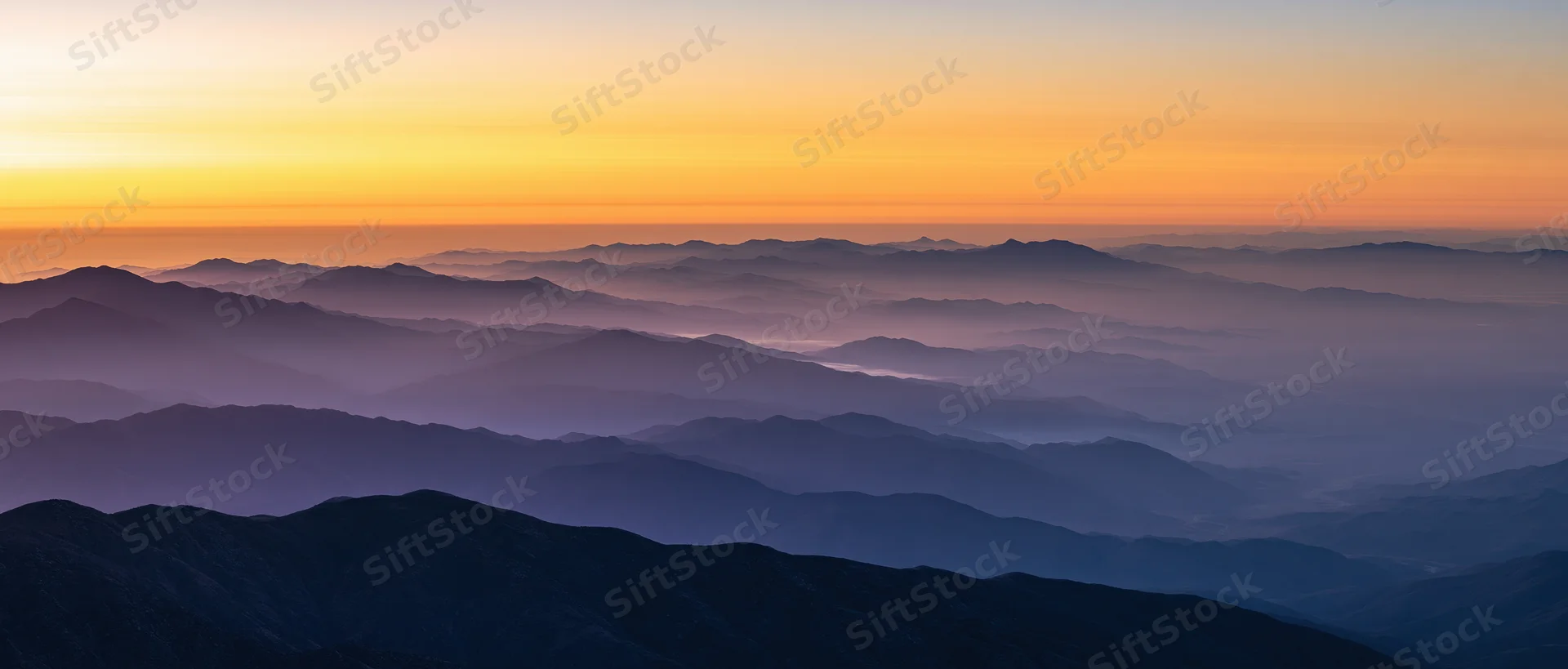 Layered mountain ridges receding into haze under a gradient sunset sky
