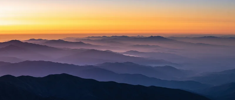 Layered mountain ridges receding into haze under a gradient sunset sky