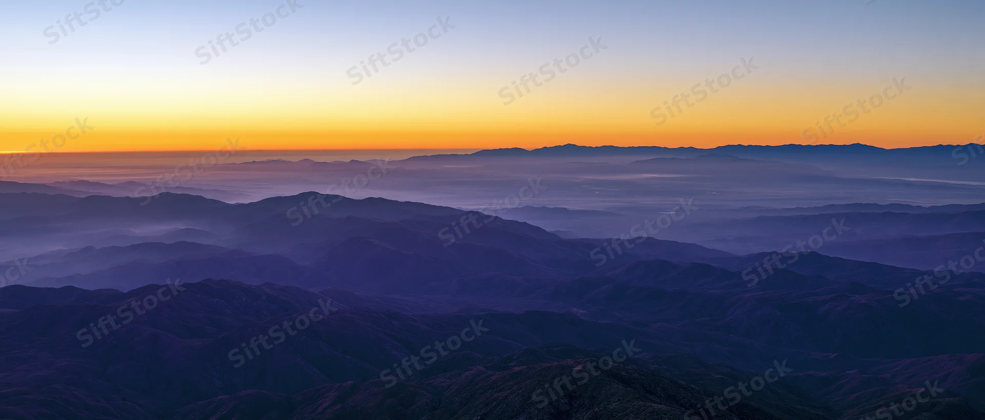 Layered mountain ranges under a gradient sunset sky with fog in the valleys