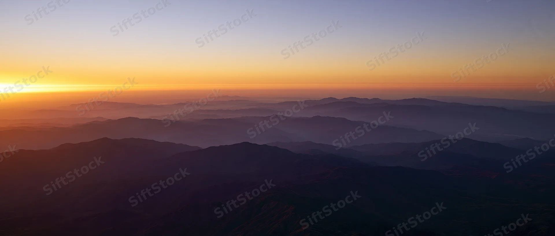 Layered mountain ranges at sunrise viewed from above with mist in the valleys