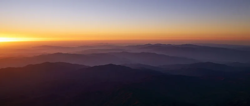 Layered mountain ranges at sunrise viewed from above with mist in the valleys