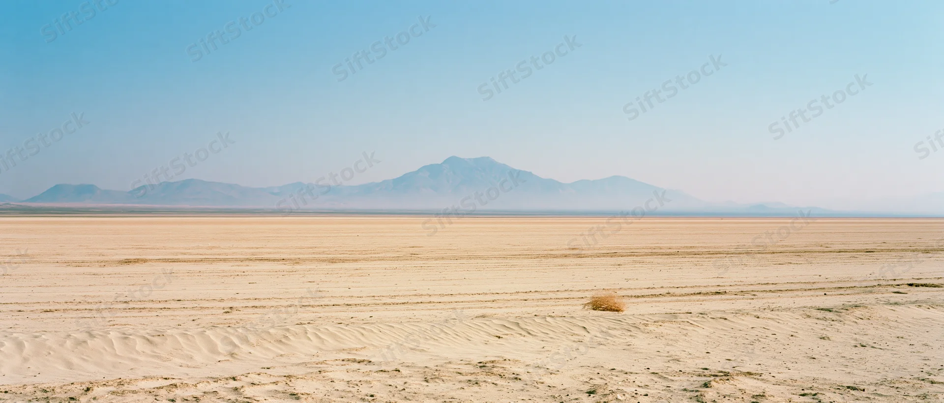 Vast desert landscape with distant mountains under clear blue sky