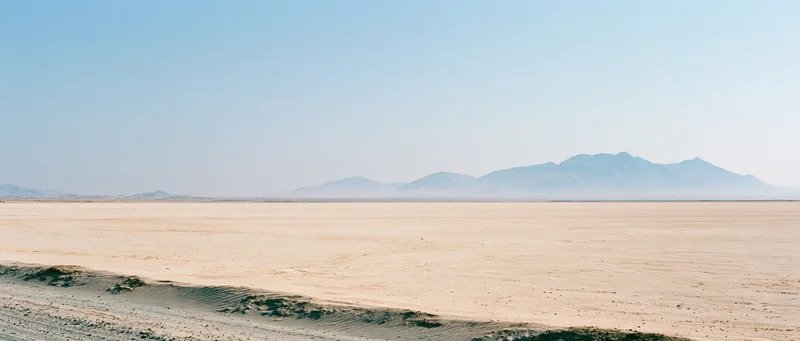Vast desert landscape with distant mountains under clear blue sky