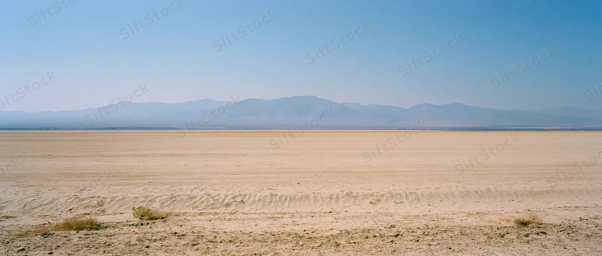 Vast sandy desert plain stretching to distant mountains under clear blue sky