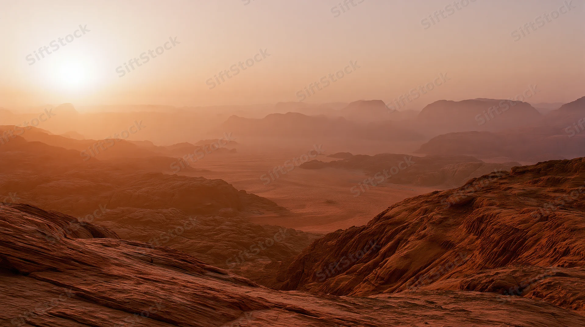 Desert canyon landscape at sunset with layered rock formations and distant mountains under warm orange sky