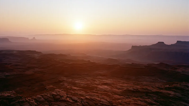Red rock canyon landscape at sunset with layered formations and distant horizon