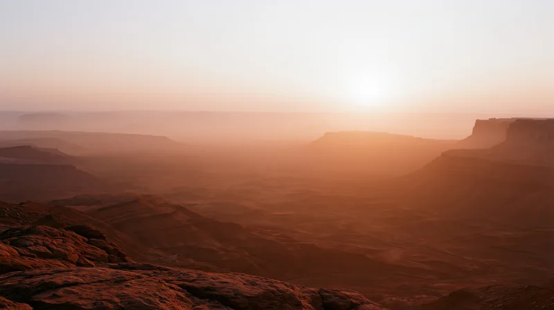 Red rock canyon landscape at sunset with layered mesas and hazy horizon