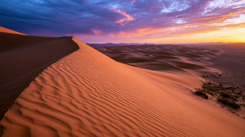 Sand dunes with rippled texture under a colorful sunset sky in a desert landscape