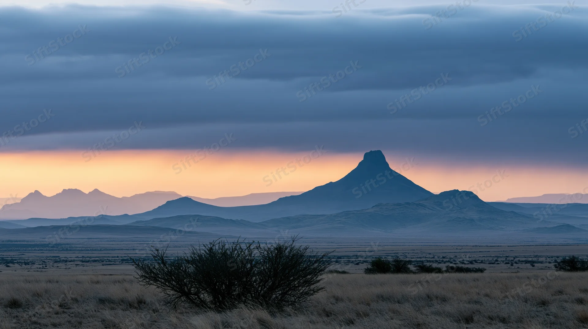 Silhouetted mountain formation at sunset over arid desert landscape with sparse scrub and distant ridges