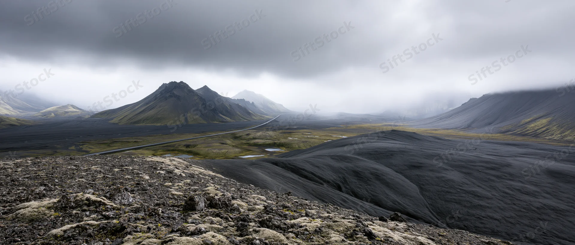 Volcanic landscape with black lava fields and winding road through misty highlands in Iceland